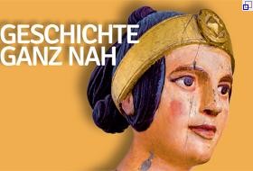 Fahnenmotiv: Ausschnit mit bemaltem Frauenkopf aus Holz und der Beschriftung "Geschichte ganz nah"