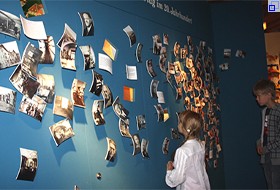 Im Schreiber-Museum betrachten 2 Kinder eine große Wand mit vielen Fotos.