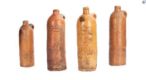 Vier hellbraune Flaschen mit schmalen Hals und Henkel. Auf jeder Flasche ist ein Stempel des jeweiligen Quellortes aufgedruckt.
