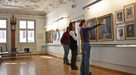 Zwei Besucherinnen und ein Besucher betrachten und diskutieren Porträtgemälde im Patrizierzimmer des Stadtmuseums im Gelben Haus.