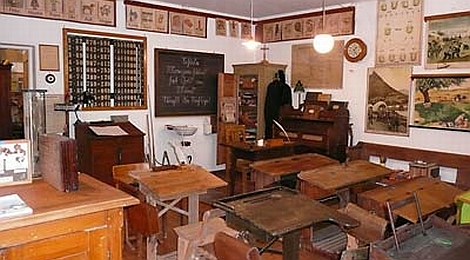 Ausstellungsraum im Schulmuseum Sulzgries: Im Schulzimmer stehen Reihen von alten Schulbänken und das Lehrerpult. An der Wand hängen Schultafeln.