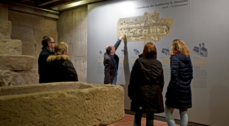Im Museum St. Dionys - Mittelalterliche Ausgrabungen: Auf einem großen Grundriss an der Wand erklärt ein Mann Teilnehmerinnen und Teilnehmern einer Führung die Baugeschichte der Kirche.