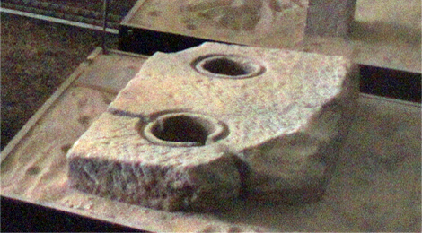 Beschädigter Stein mit zwei runden Löchern.