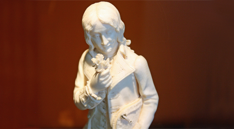 Einfarbige geschnitzte Elfenbeinfigur: Ein junger Mann mit längeren Haaren. Er trägt eine Jacke mit breitem Kragenaufschlag. In der rechten Hand hält er einen kleinen Blumenstrauß.