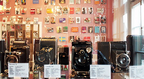 Eine Vitrine mit alten Fotoapparaten, dahinter eine Wand mit zahlreichen Postkarten.